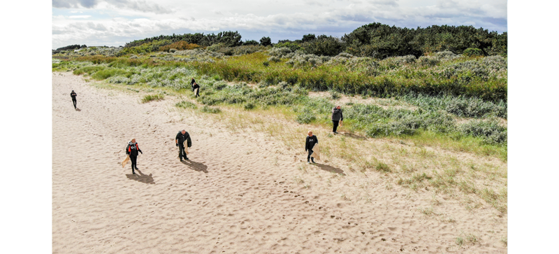 Am Strand sind mehrere Leute, die am Strand aufräumen. 