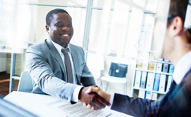 Zwei Männer sitzen sich im Büro gegenüber und geben sich die Hand