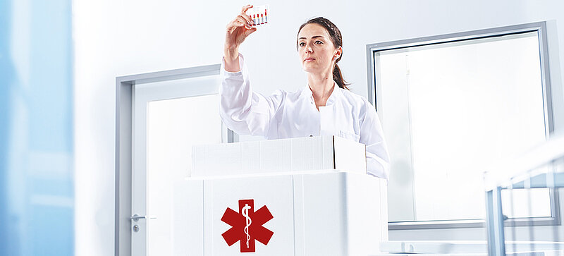 Eine Frau entnimmt aus einer Isolierbox ein Reagenzglas